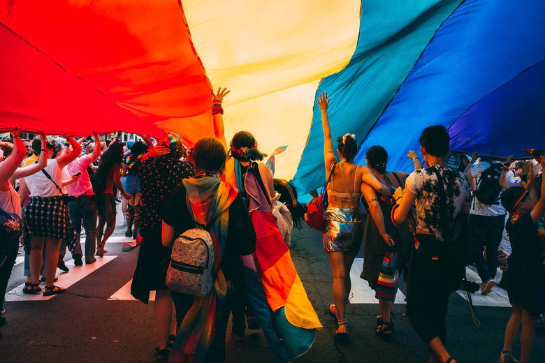 People under a rainbow flag at Pride