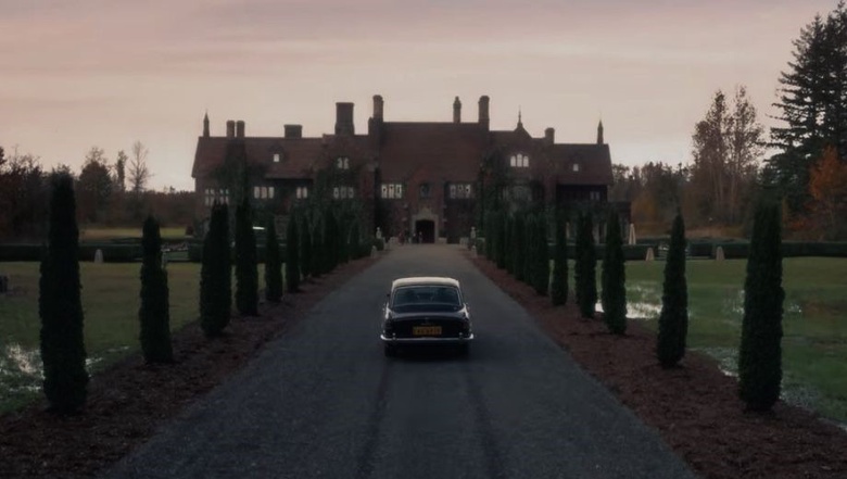 A creepy, dimly lit scene with a car approaching an old looking manor house