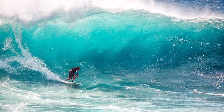 Man surfs on a huge bright blue wave