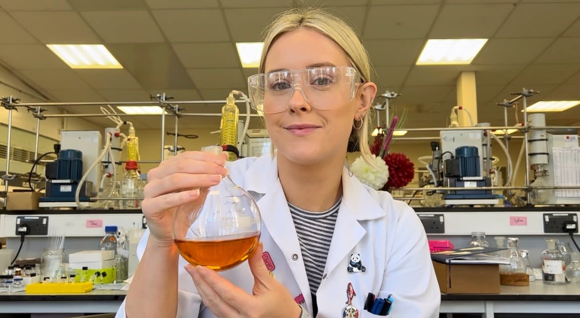 Dr Jessica Gomez-Banderas in a laboratory holding up a beaker containg an orange liquid