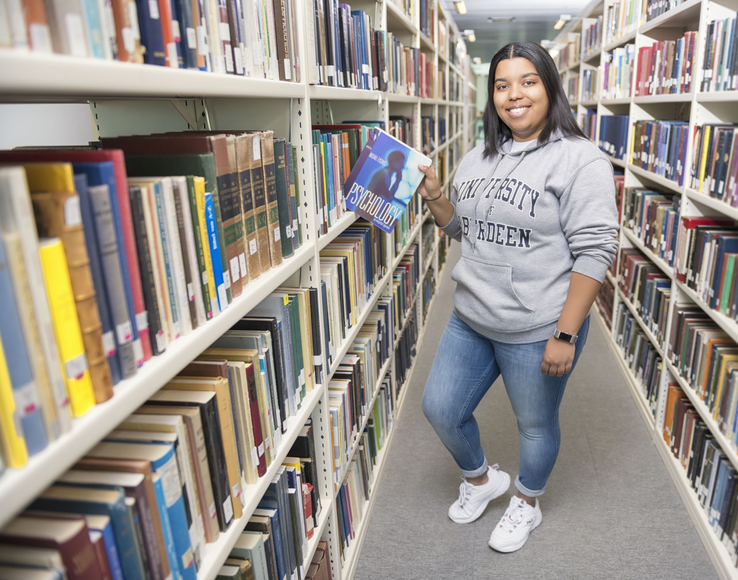 Photo of Marta Lopes standing next to a bookshelf in the Duncan Rice Library.