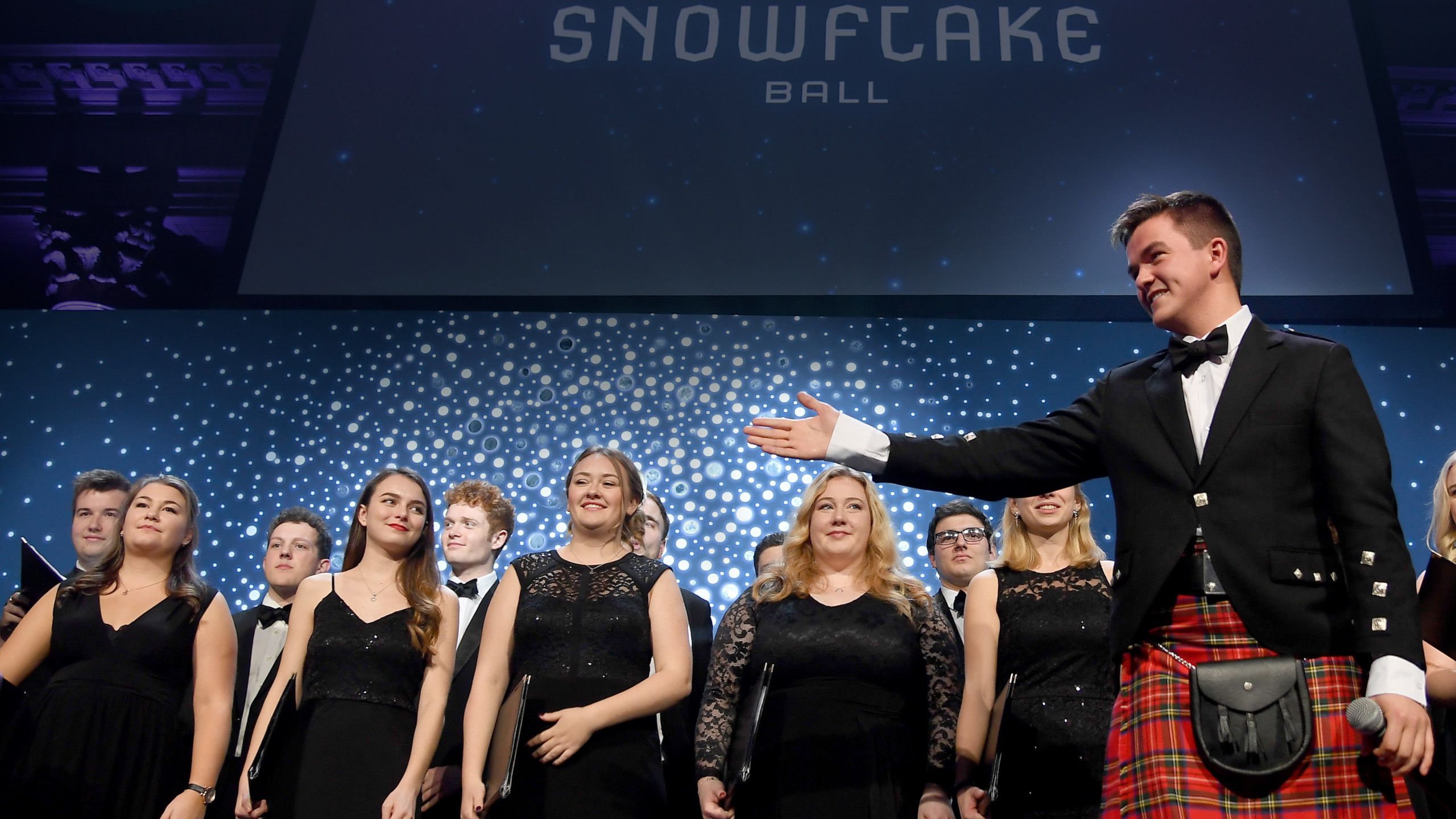 Photo of Peter MacPherson (right) on stage with the University Chapel Choir.