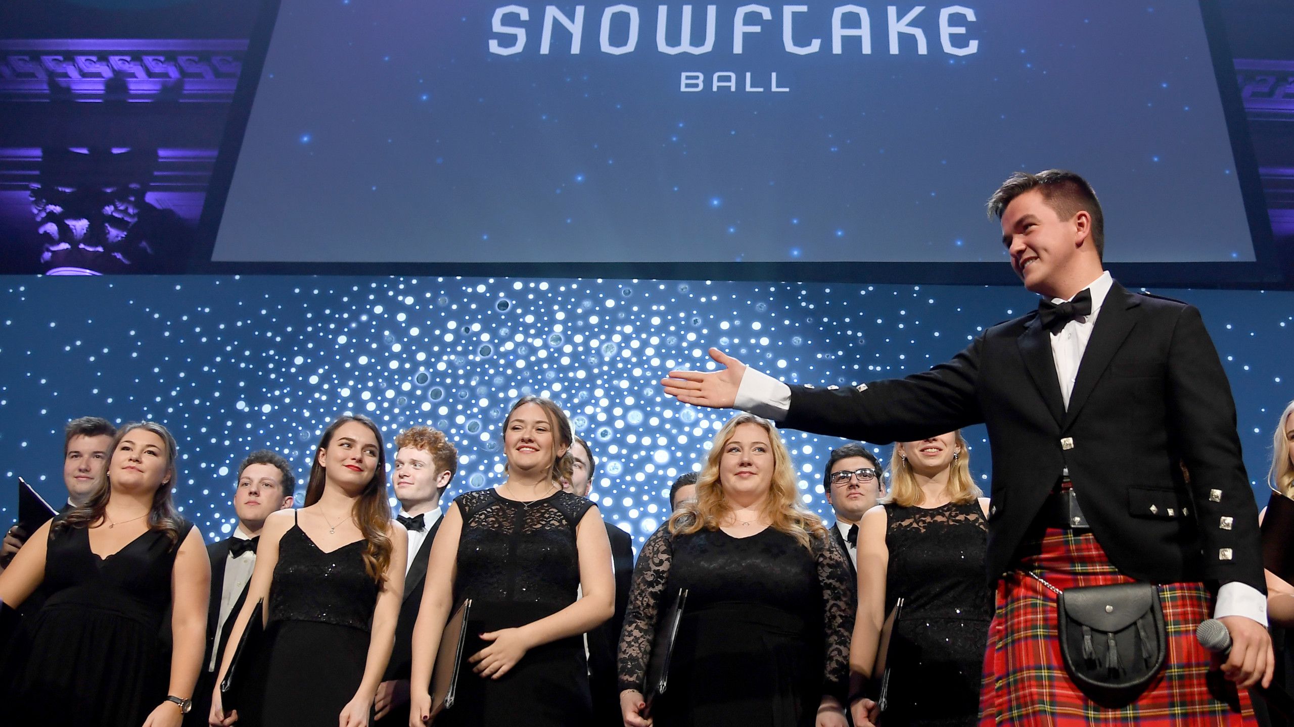 Photo of Peter MacPherson (right) on stage with the University Chapel Choir.
