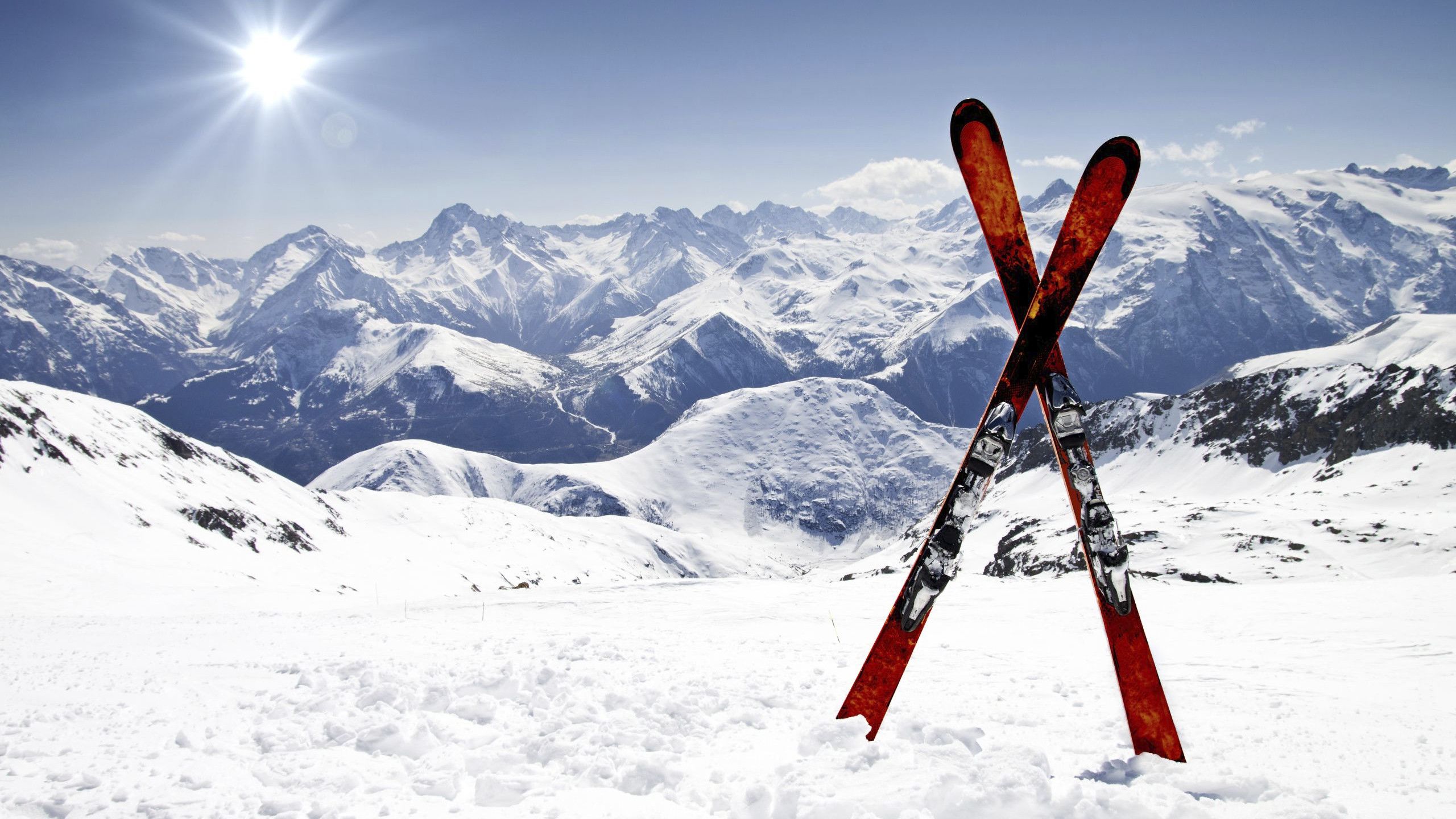 Photo of a pair of skis, with snowy mountains in the background.