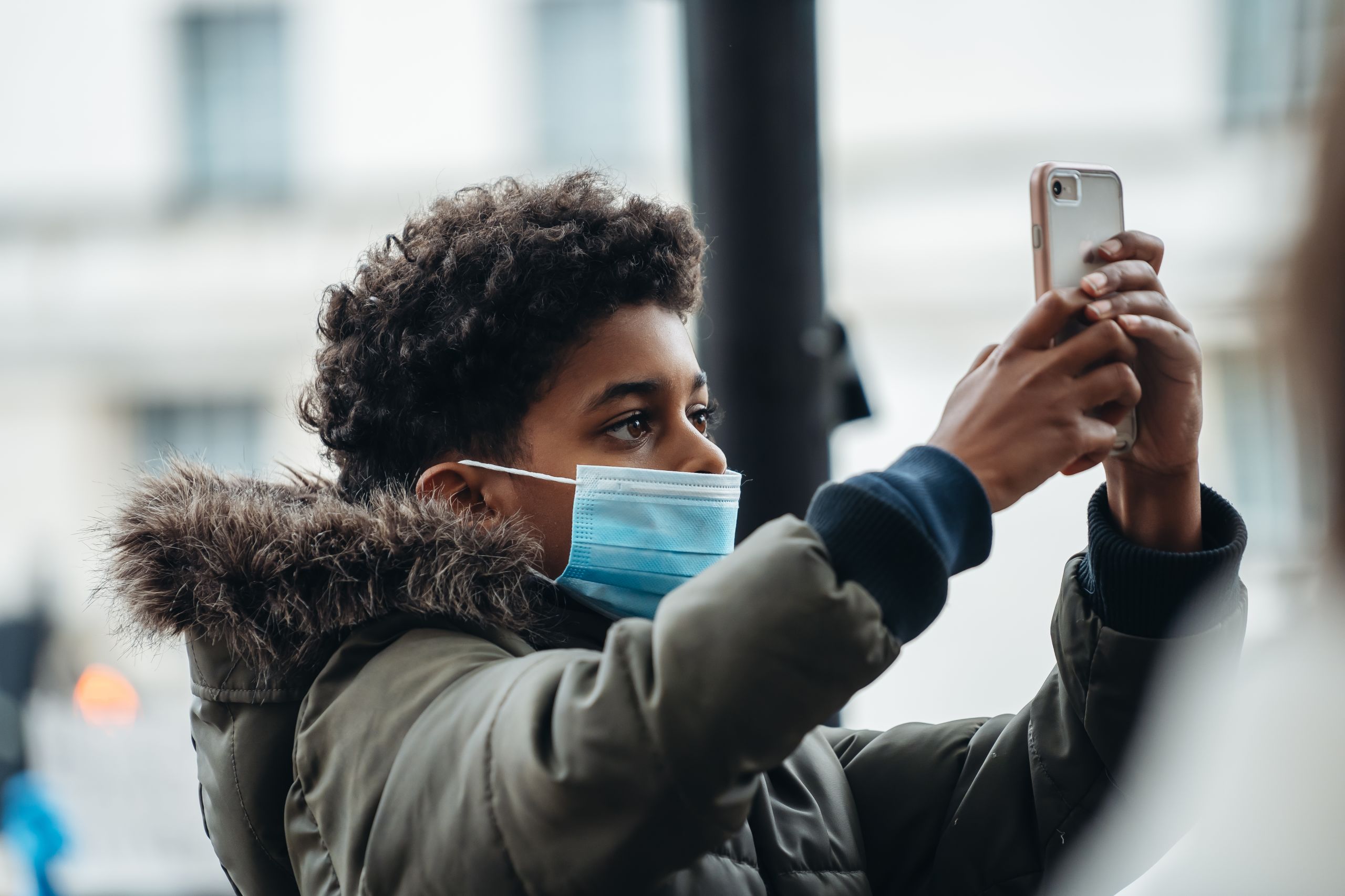 A boy with a face mask is filming with his smartphone.